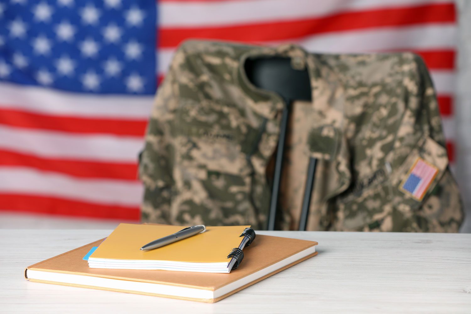 Featured image for GI Bill showing notebooks on a table with a soldier uniform and a flag of the United States in the background