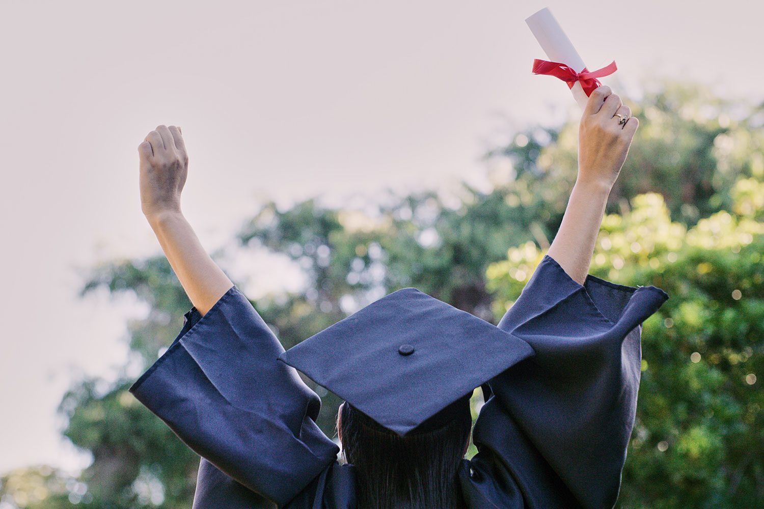 Featured image for Military Spouse Scholarships, showing a female student during graduation celebrating and holding a diploma