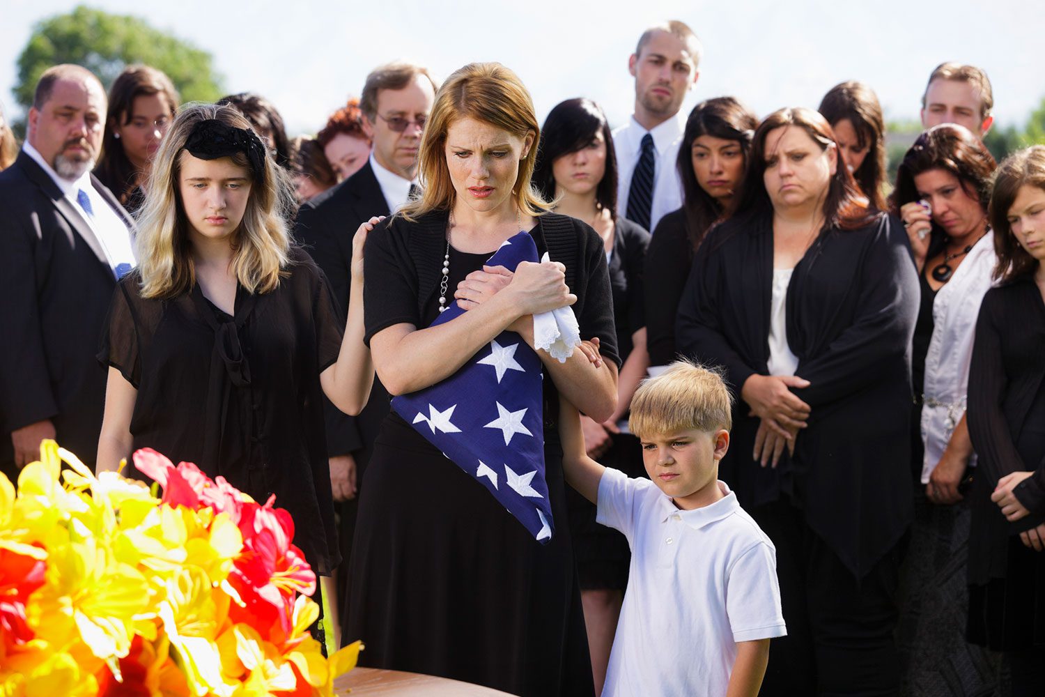 Featured image for VA Survivor Benefits, showing a grieving widow and her children at a military funeral