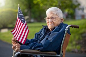 Featured image for TRICARE for Retired Military Members, showing a Veteran in a wheelchair with a flag of the United States in his hands